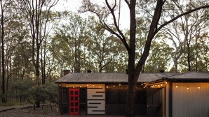 A small, rustic cabin with a red door, surrounded by trees. - Pokolbin Cottages (Pokolbin)