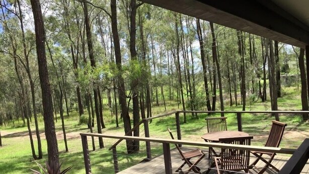 A wooden deck with outdoor furniture, surrounded by a forest. - Pokolbin Cottages (Pokolbin)