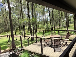 A wooden deck with outdoor furniture, surrounded by a forest. - Pokolbin Cottages (Pokolbin)