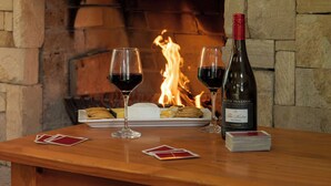 A wooden table with two glasses of red wine, a bottle of wine, and playing cards. - Pokolbin Cottages (Pokolbin)