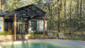 A covered outdoor pool area with a wooden deck, a bench, and a fence. - Pokolbin Cottages (Pokolbin)