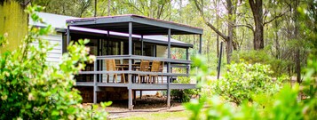 A two-story wooden cabin with a balcony, surrounded by dense forest.
