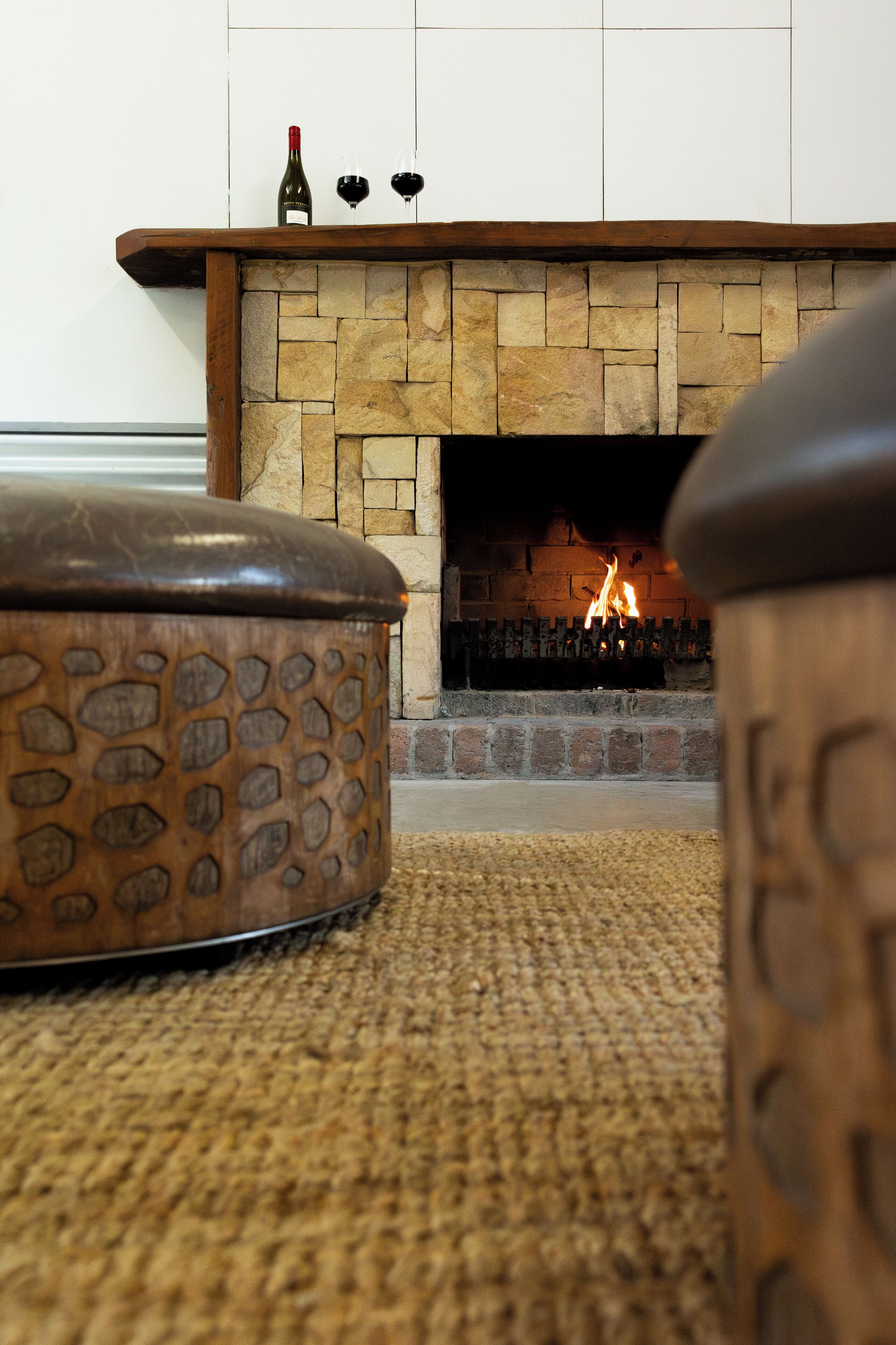 Una chimenea de piedra con fuego, un fuste de madera y una botella de vino.