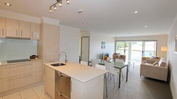 A modern kitchen with a central island, a dining area with a glass table, and a living room with a sofa and chairs.