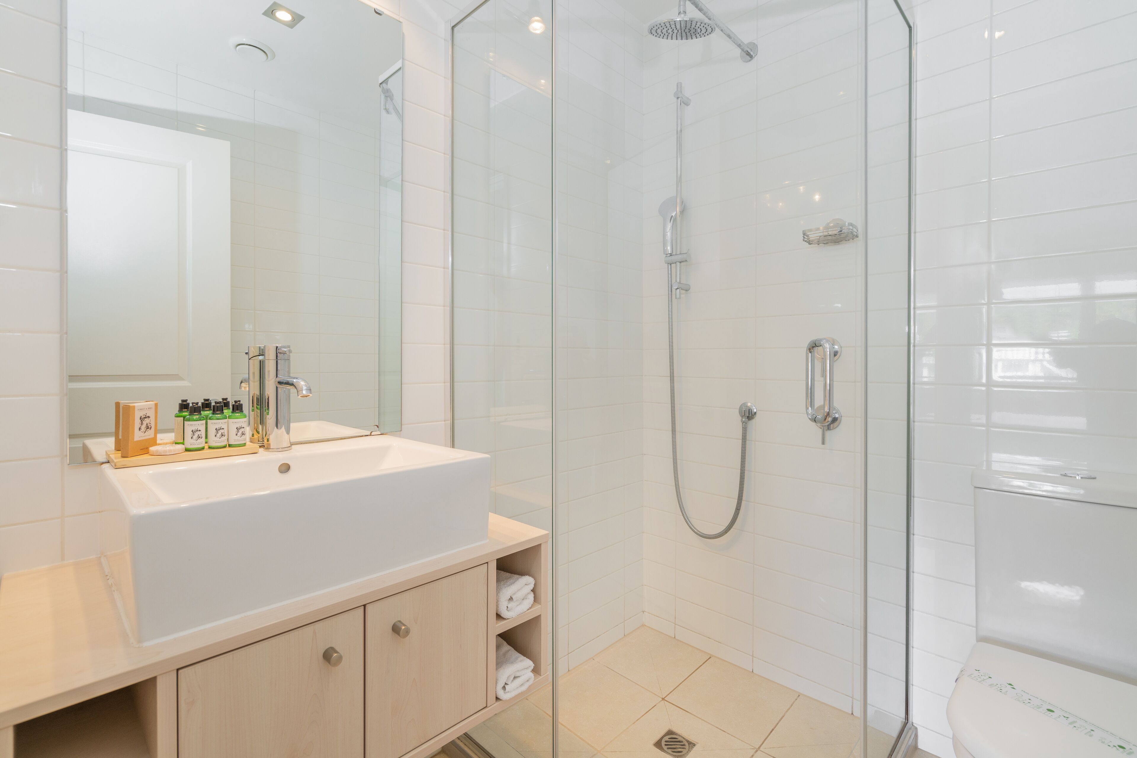 Un baño moderno con ducha de vidrio, lavabo blanco con tocador y espejo sobre el lavabo.