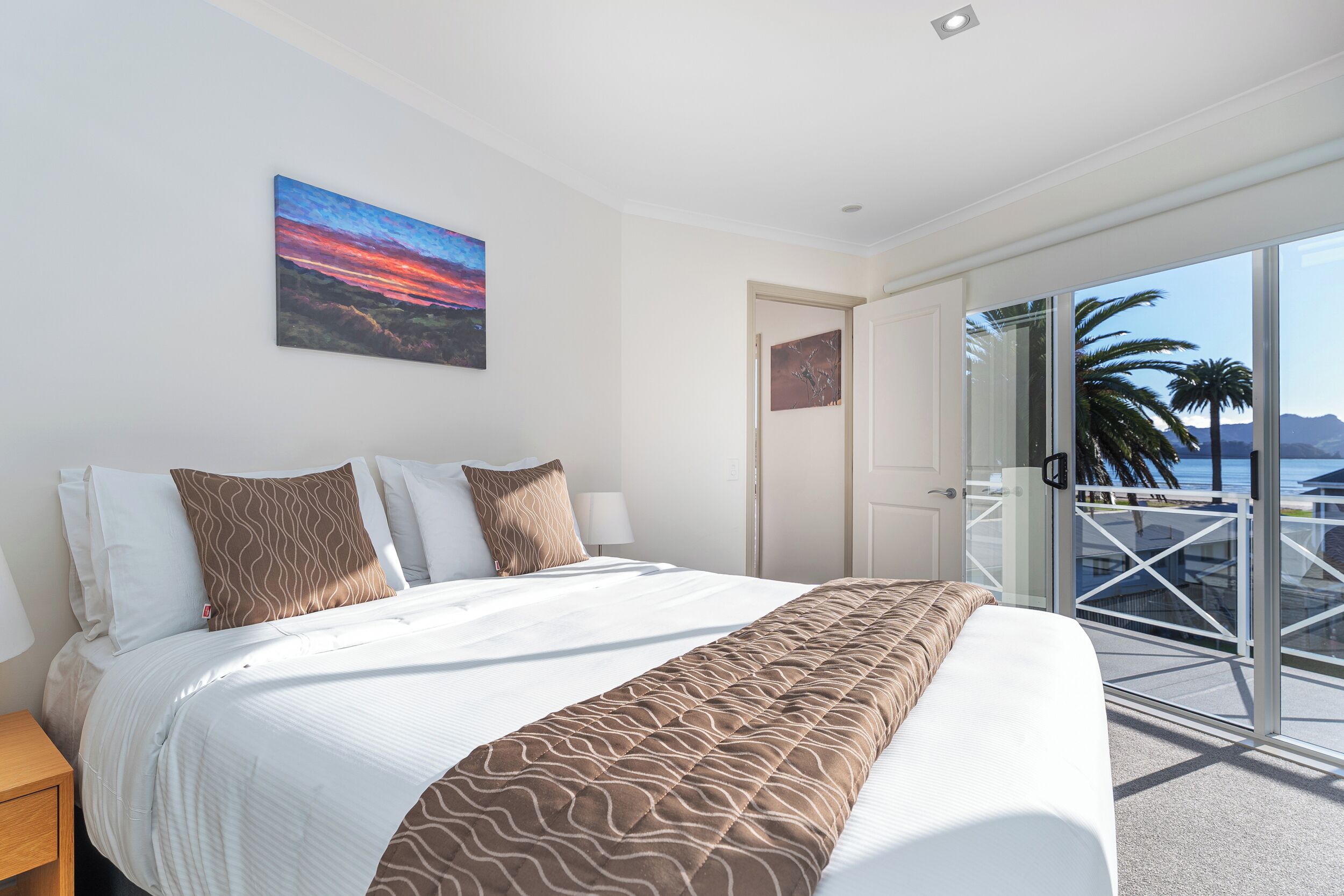 Habitación de hotel con una cama grande, vistas al mar y un balcón con puerta de cristal.