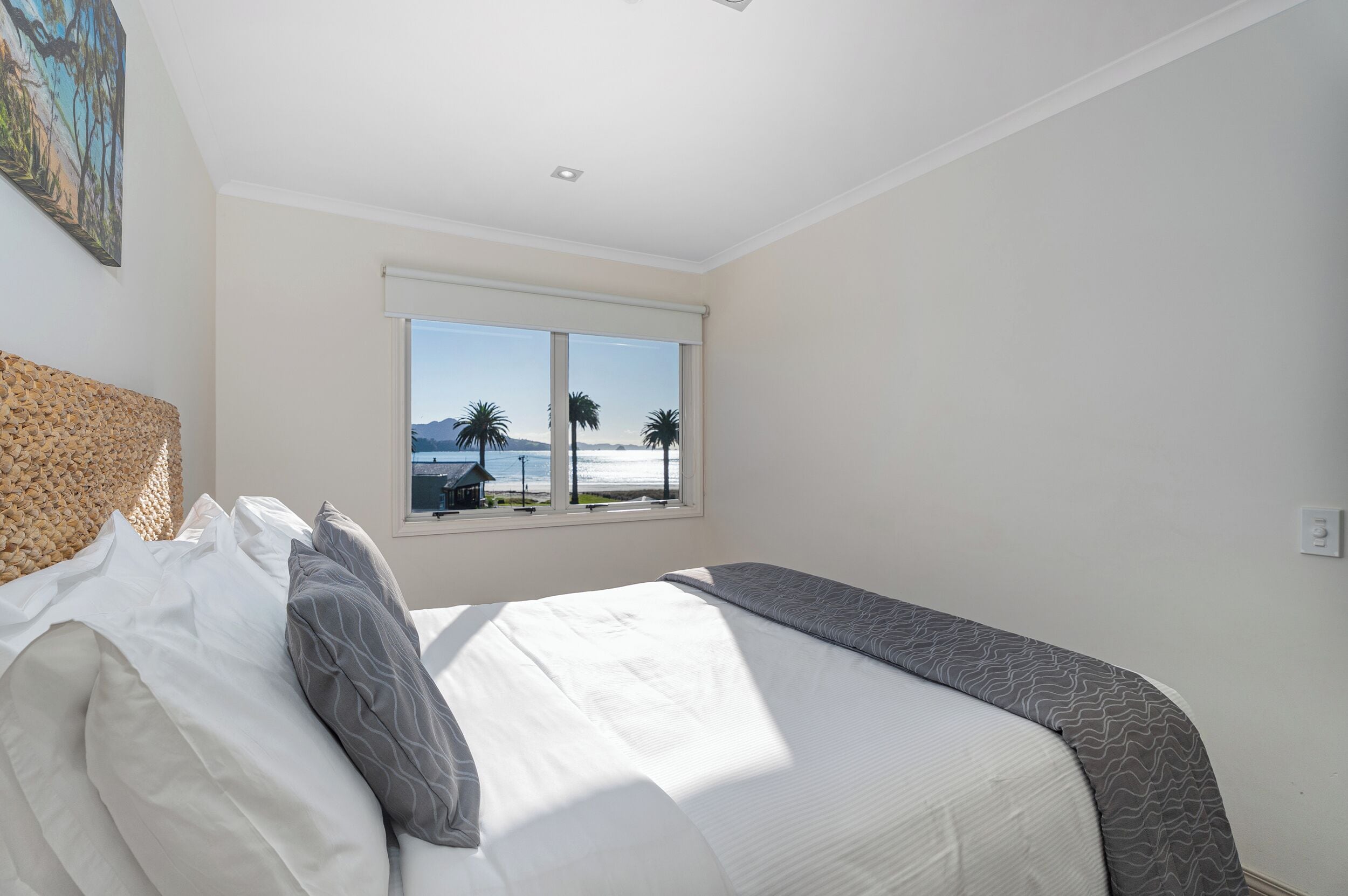 A bedroom with a large bed, a view of the beach, and a ceiling light.