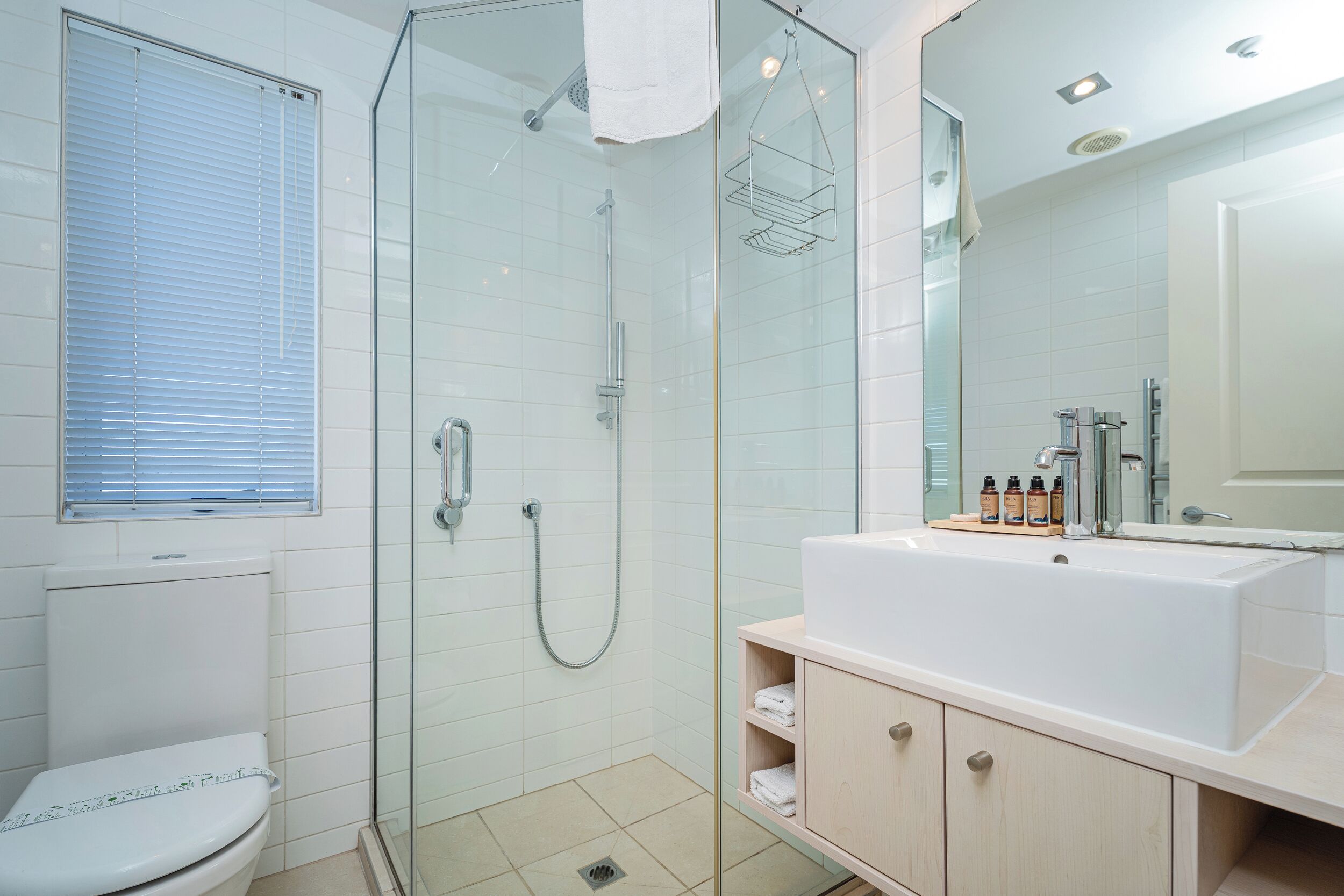 A modern bathroom with a glass-enclosed shower, a large white sink, and a wooden vanity.