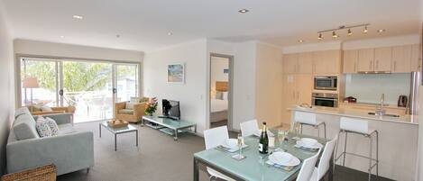 A modern living room with a sofa, TV, and dining area with chairs and a table set for a meal.