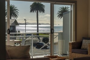 Un balcón con vista al mar, palmeras y coches aparcados.