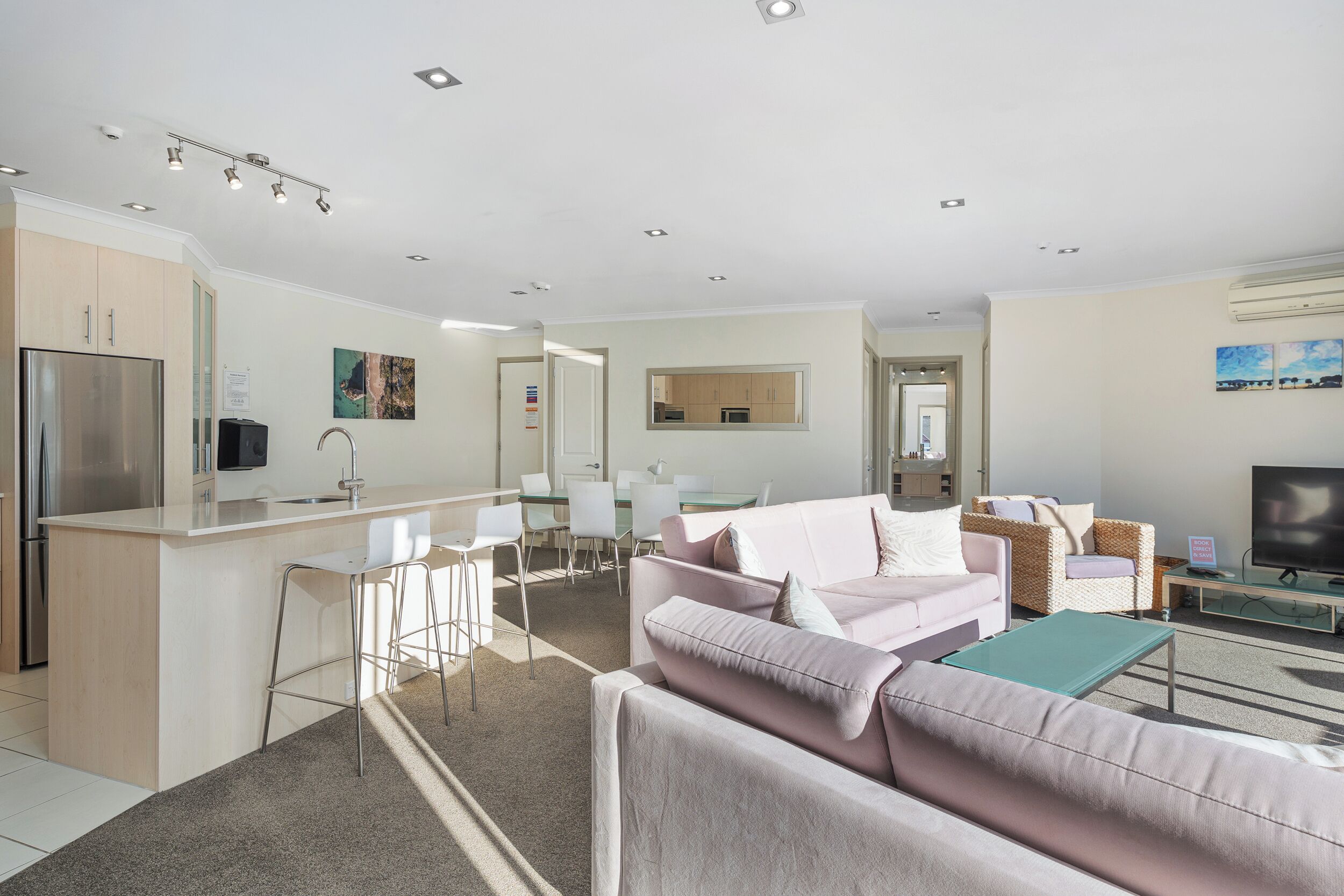Una sala de estar moderna con un sofá, una mesa de centro y un televisor. Cuenta con una zona de cocina con un refrigerador y una mesa de comedor.