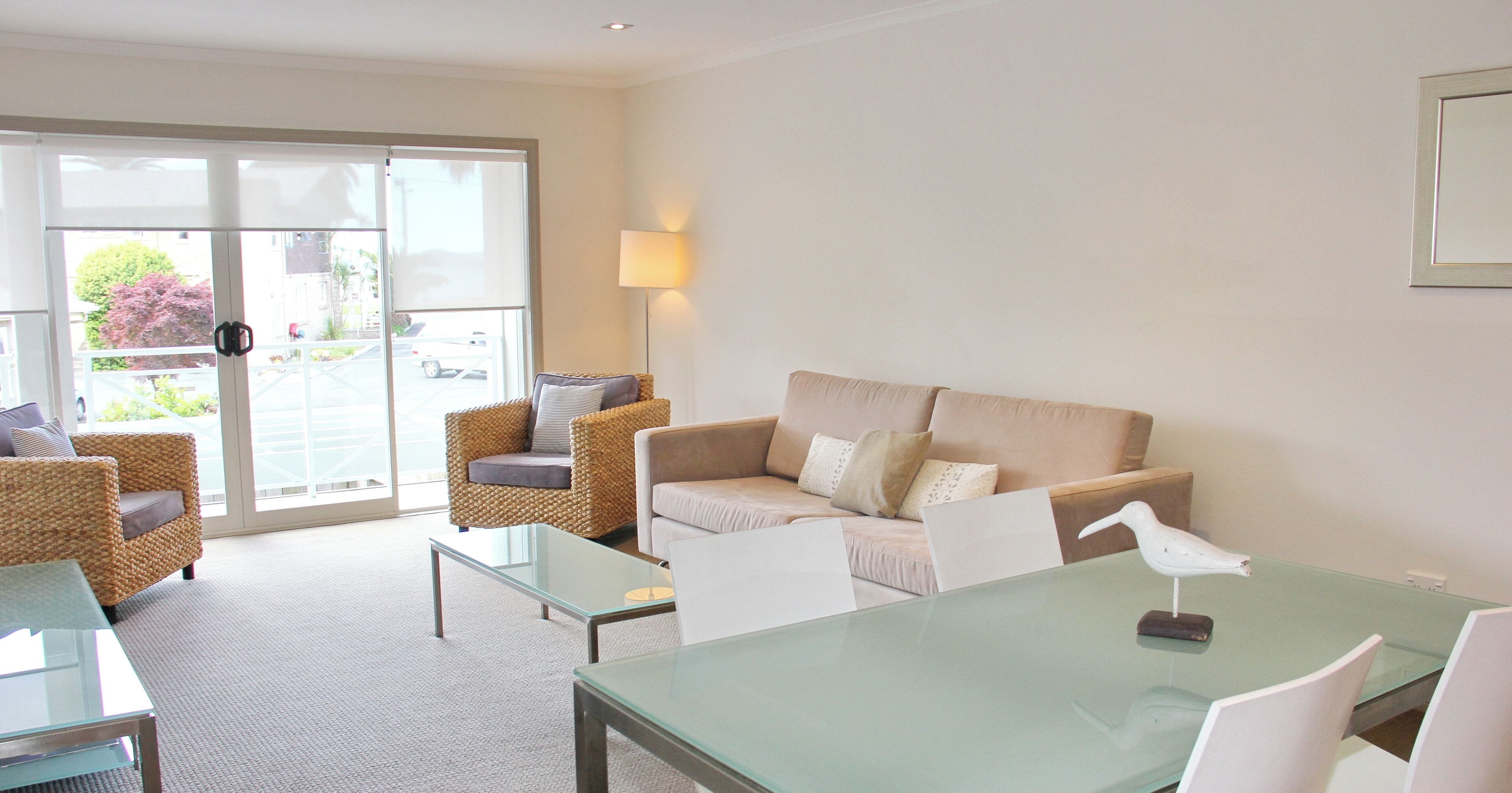 A living room with a glass coffee table, two wicker sofas, a beige sofa, and a white chair.