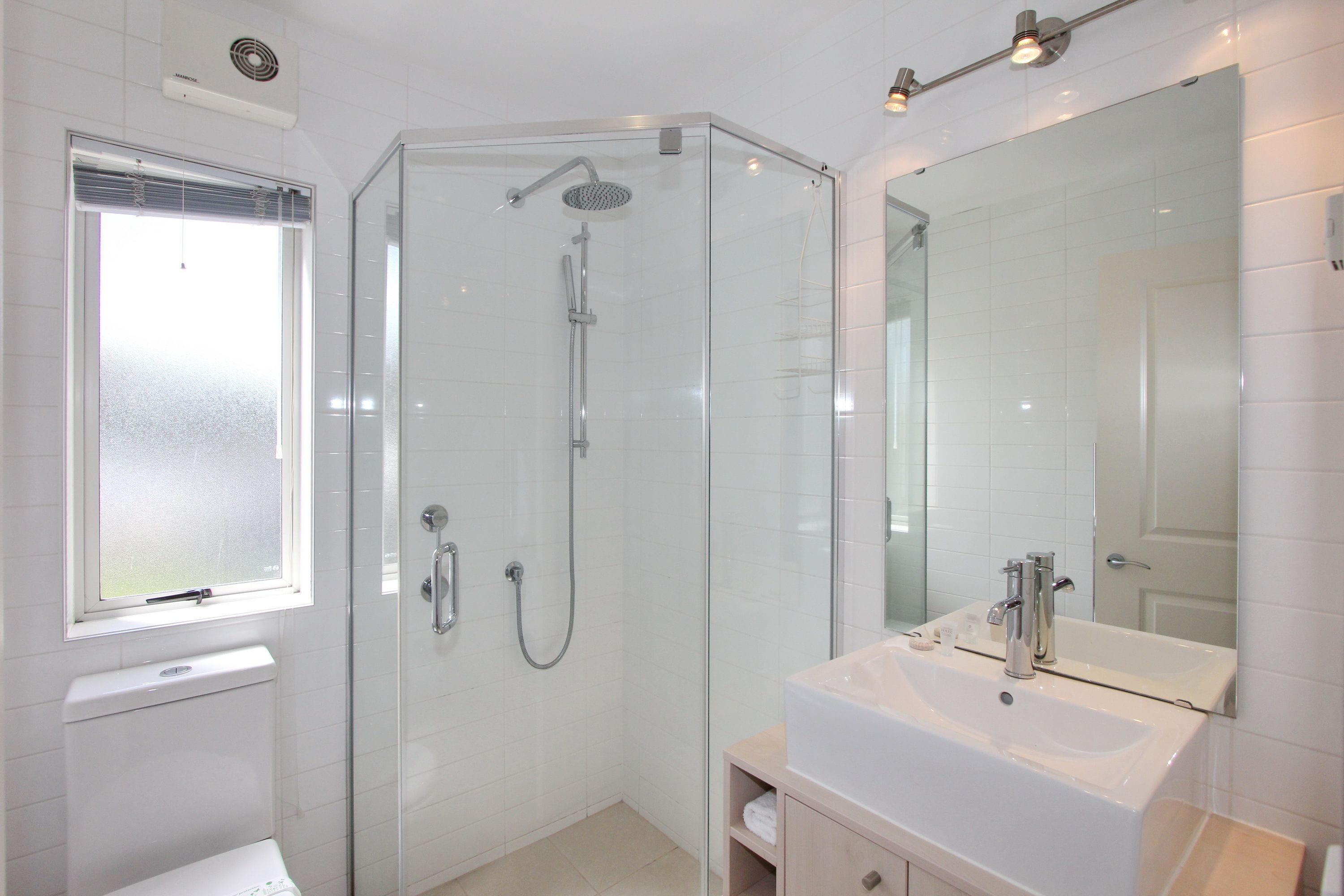Un baño moderno con ducha de mampara de vidrio, un lavabo blanco y un espejo grande.