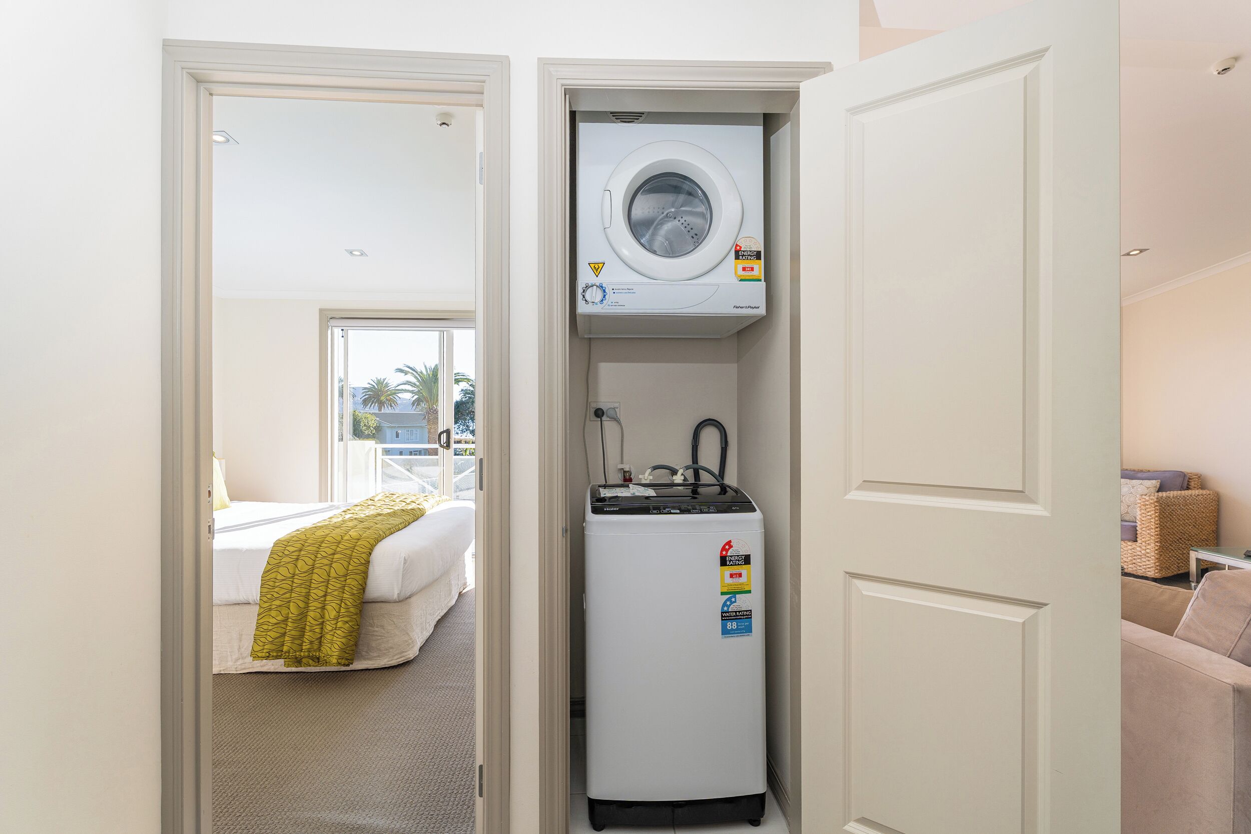 A compact hotel room with a bed, a washing machine, and a small refrigerator.
