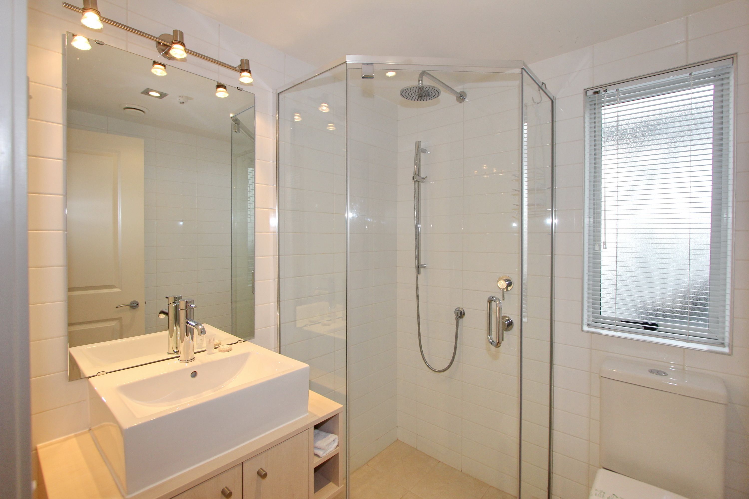 A modern bathroom with a glass-enclosed shower, a white sink, and a large mirror.