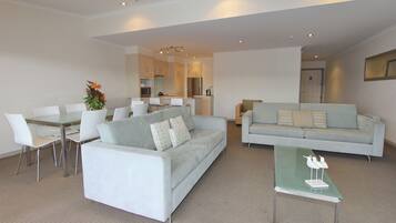 A modern living room with a grey sofa, a dining table with chairs, and a kitchen in the background.