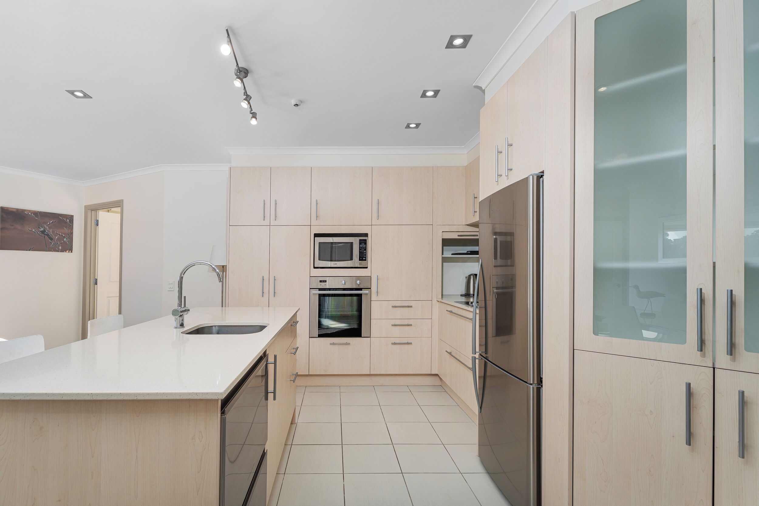 A modern kitchen with light wood cabinets, stainless steel appliances, and a white countertop.