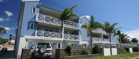 A two-story hotel with a blue exterior, a balcony on the second floor, and a stone wall with the name 'CROW' in front.