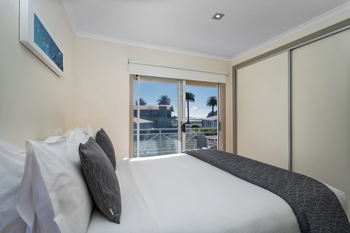 Habitación de hotel con una cama grande, vistas a palmeras y un edificio a través de una puerta corrediza, y un cuadro en la pared.
