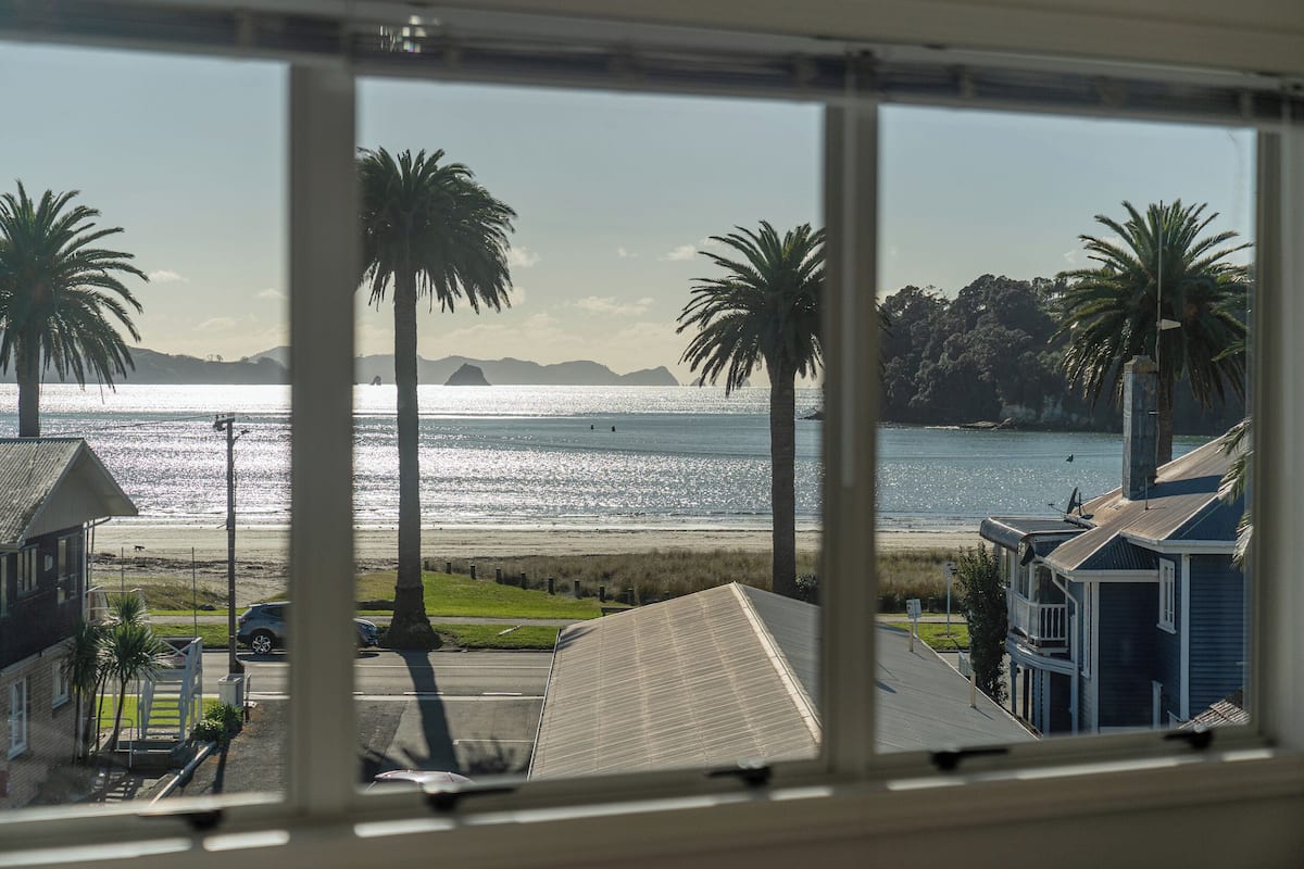 Vista costera desde una ventana con vista a una playa, palmeras, una carretera y edificios residenciales.