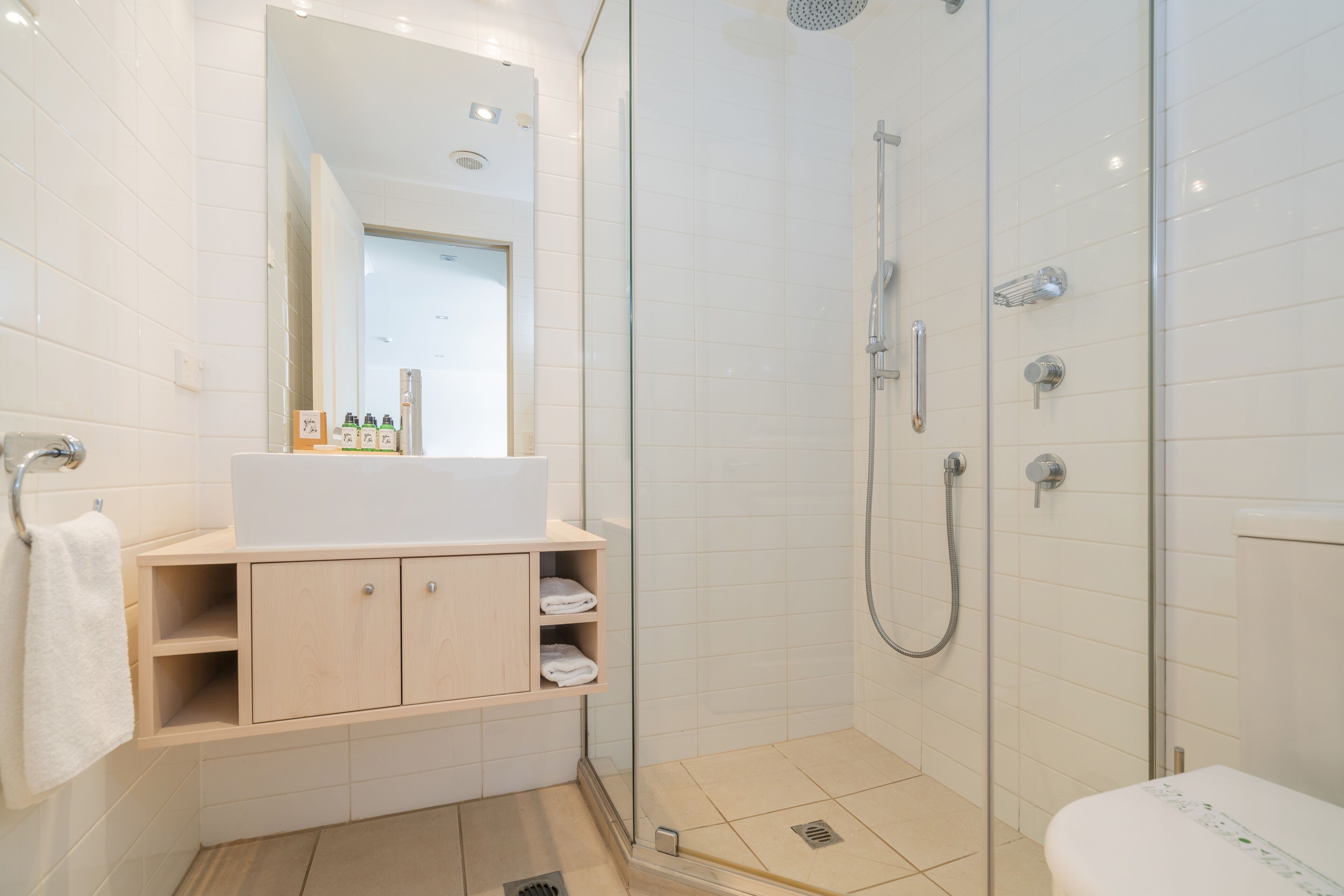 A modern bathroom with a glass-enclosed shower, a white sink with a mirror above, and wooden cabinets.