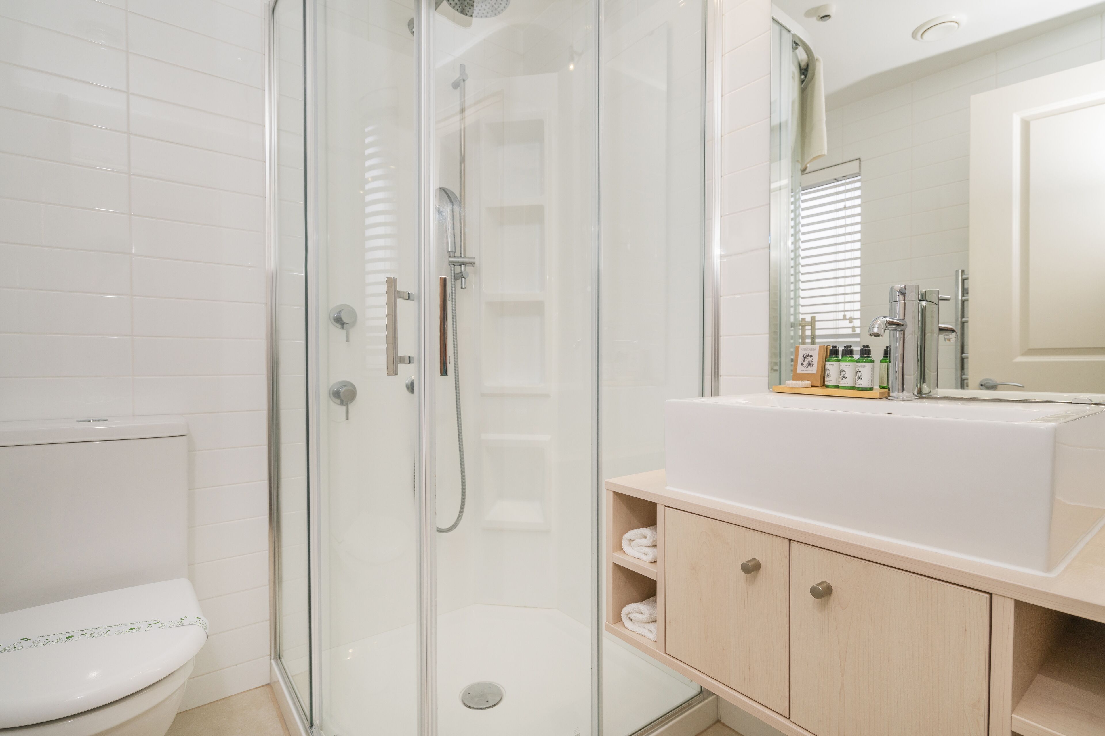 Un baño moderno con ducha de vidrio, inodoro blanco y tocador de madera con espejo.