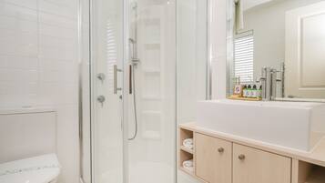 Un baño moderno con ducha de vidrio, inodoro blanco y tocador de madera con espejo.