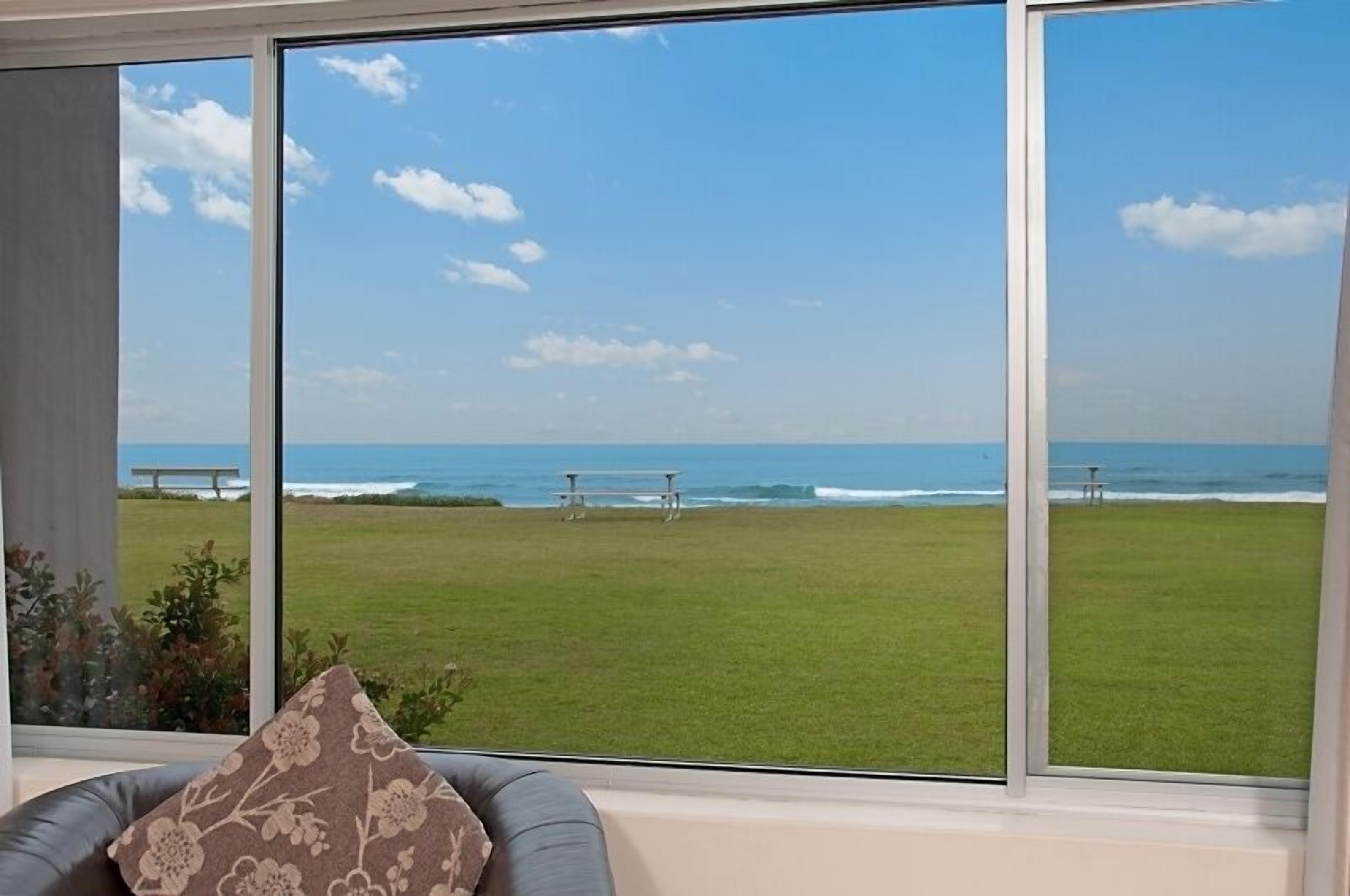 A room with large windows overlooking a grassy area and the ocean.