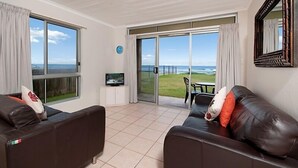 Ein Wohnzimmer mit einer großen Schiebeglasdoor, die auf einen Balkon mit Meerblick führt.