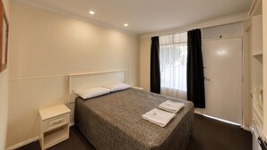Habitación de hotel ordenada con una cama individual, mesita de noche, armario y ventana con cortinas.
