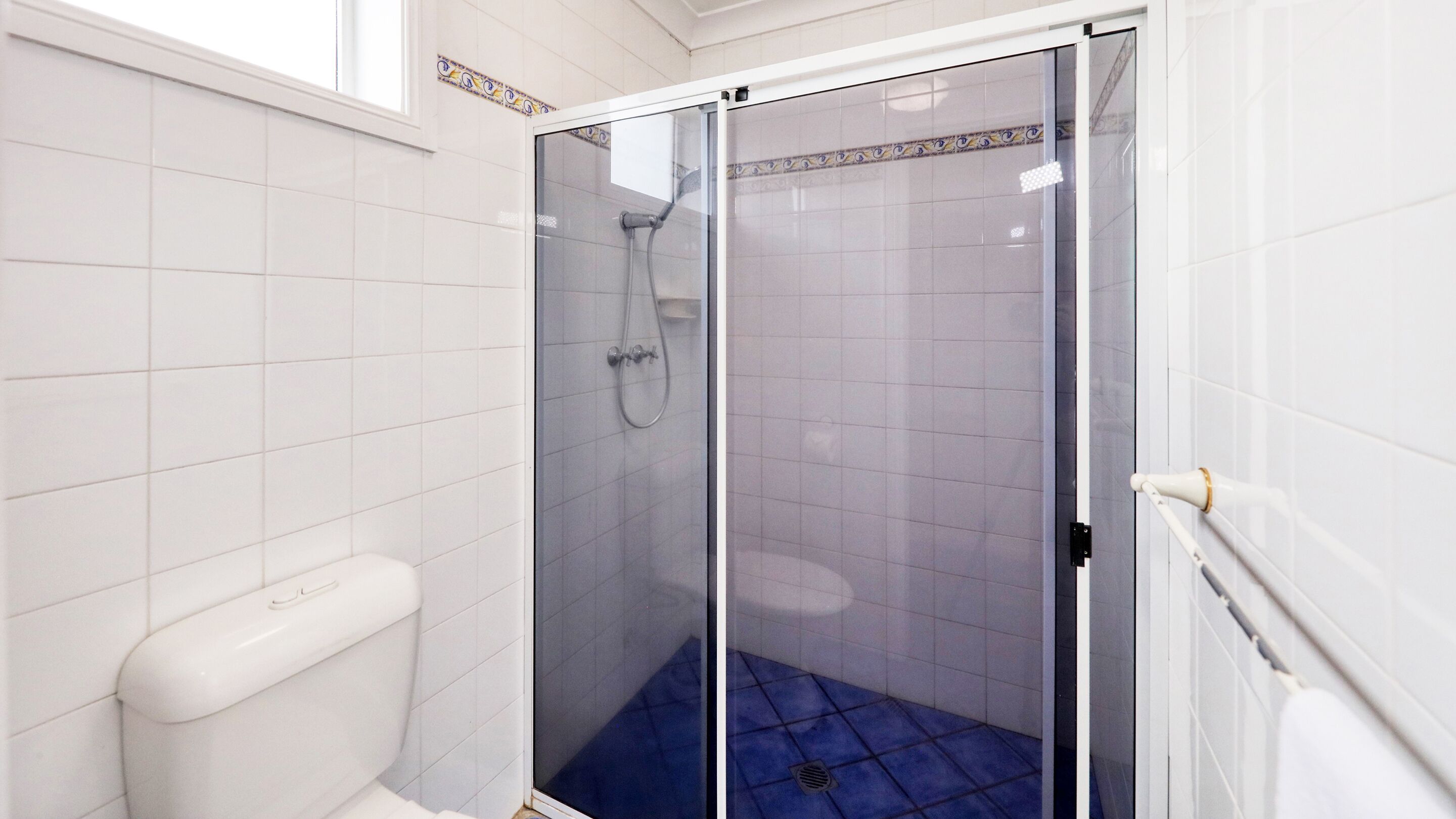Un bagno con doccia vetro, piastrelle bianche e un water.