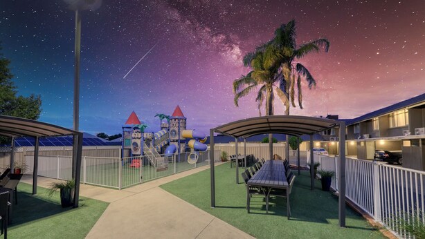Un parque infantil con toboganes y estructuras para escalar, una zona de descanso cubierta y vistas del cielo nocturno.