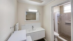 A bathroom with a white sink, mirror, and shower. - Coachman Hotel Motel (Parkes)