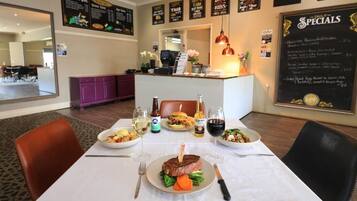 A restaurant interior with a dining table set for two, a menu board, and a counter with a cash register.