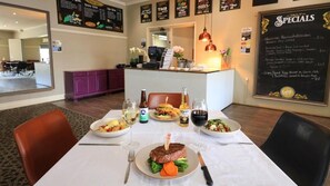 A restaurant interior with a dining table set for two, a menu board, and a counter with a cash register. - Coachman Hotel Motel (Parkes)