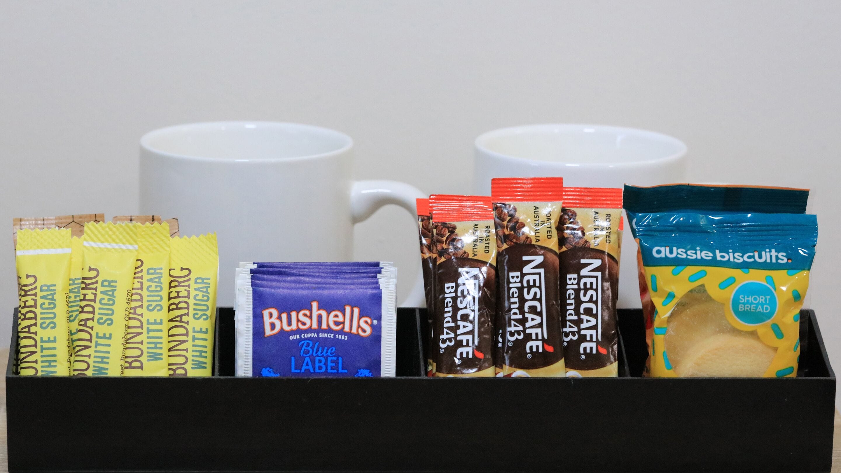 A box containing coffee pods, a coffee mug, and a packet of biscuits.