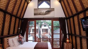 A cozy room with a bed, a wooden bench, and a view of a house through a glass door. - Mojo Resort (Canggu)