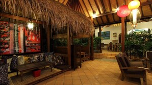 A thatched-roof lounge area with wooden furniture, a tiled floor, and hanging lamps. - Mojo Resort (Canggu)