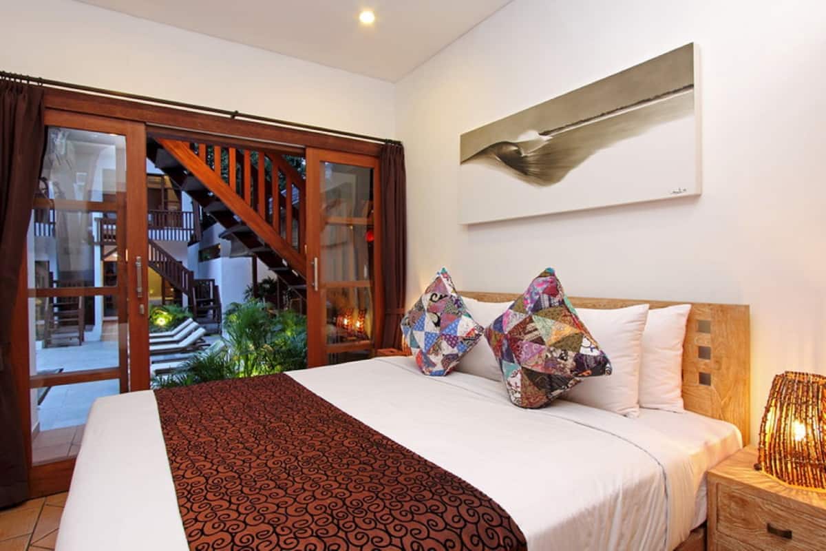 A hotel room with a bed, a wooden headboard, a large window with a view of a staircase, and a wall-mounted artwork.