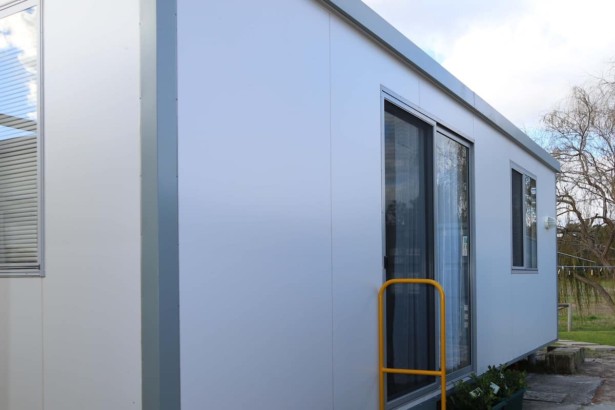 A modern, single-story building with a white exterior, large windows, and a yellow door frame.