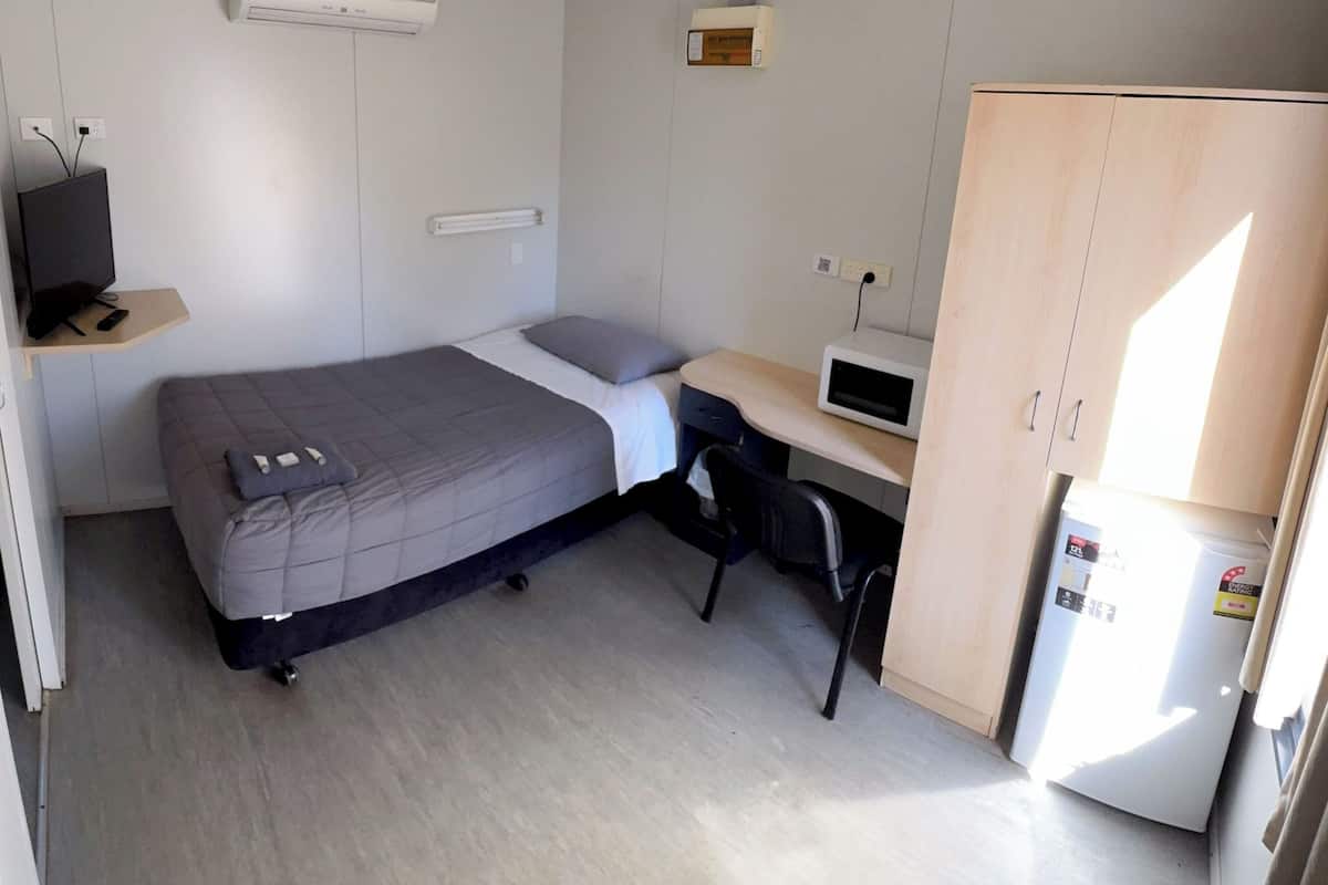 A compact room with a bed, a desk with a computer, a TV, and a refrigerator.