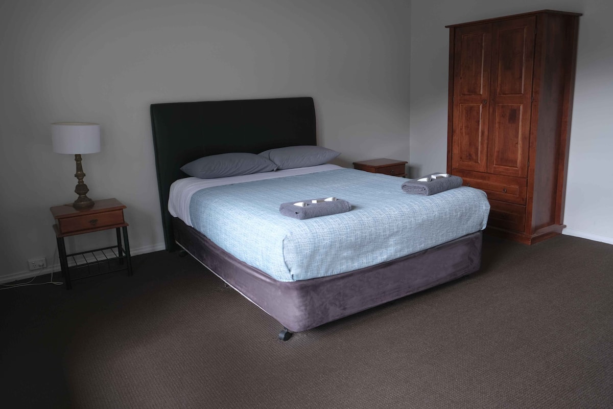 A bedroom with a bed, a nightstand, a lamp, and a wardrobe.