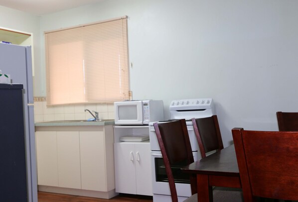 A small kitchen with a microwave, stove, and cabinets. There is a dining table with chairs.