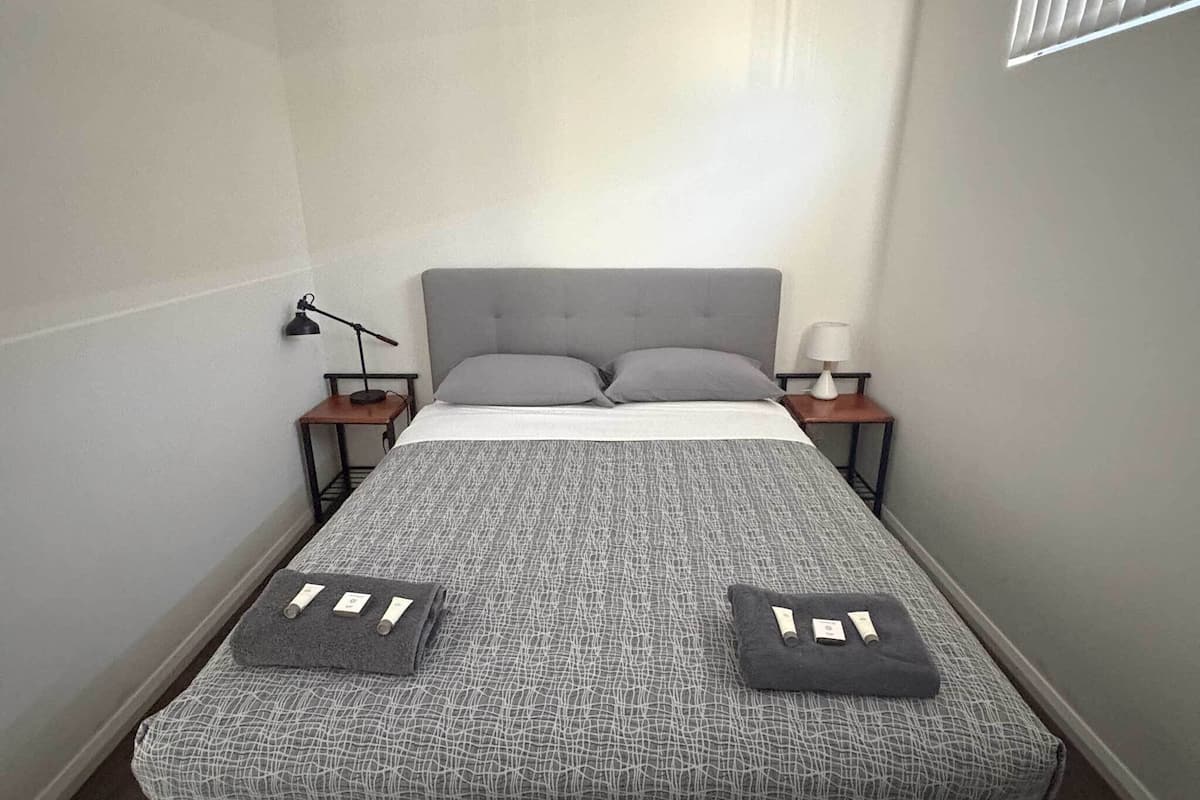 A bed with a grey upholstered headboard, two bedside tables with lamps, and a grey patterned bedspread.