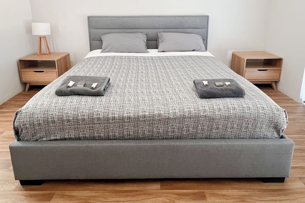 A modern bedroom with a grey upholstered bed, two bedside tables, and a nightstand with a lamp.