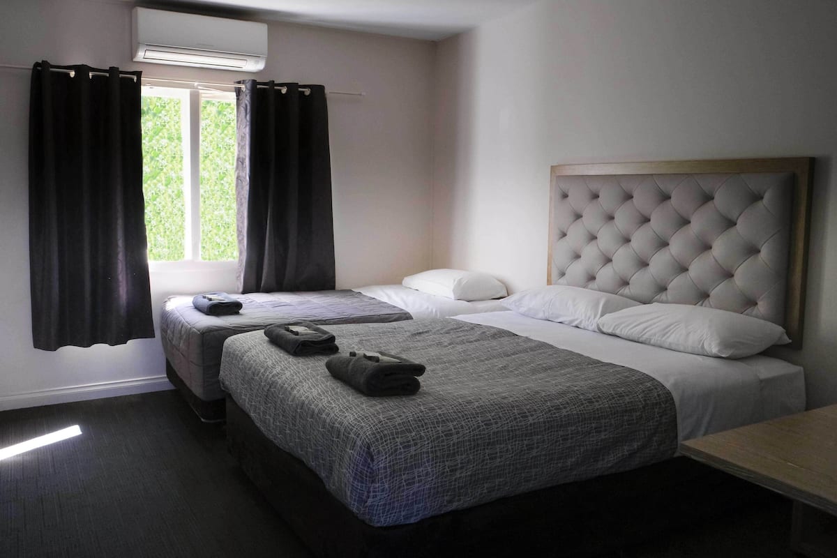 A hotel room with two beds, a window with curtains, a headboard, and a bedside table.