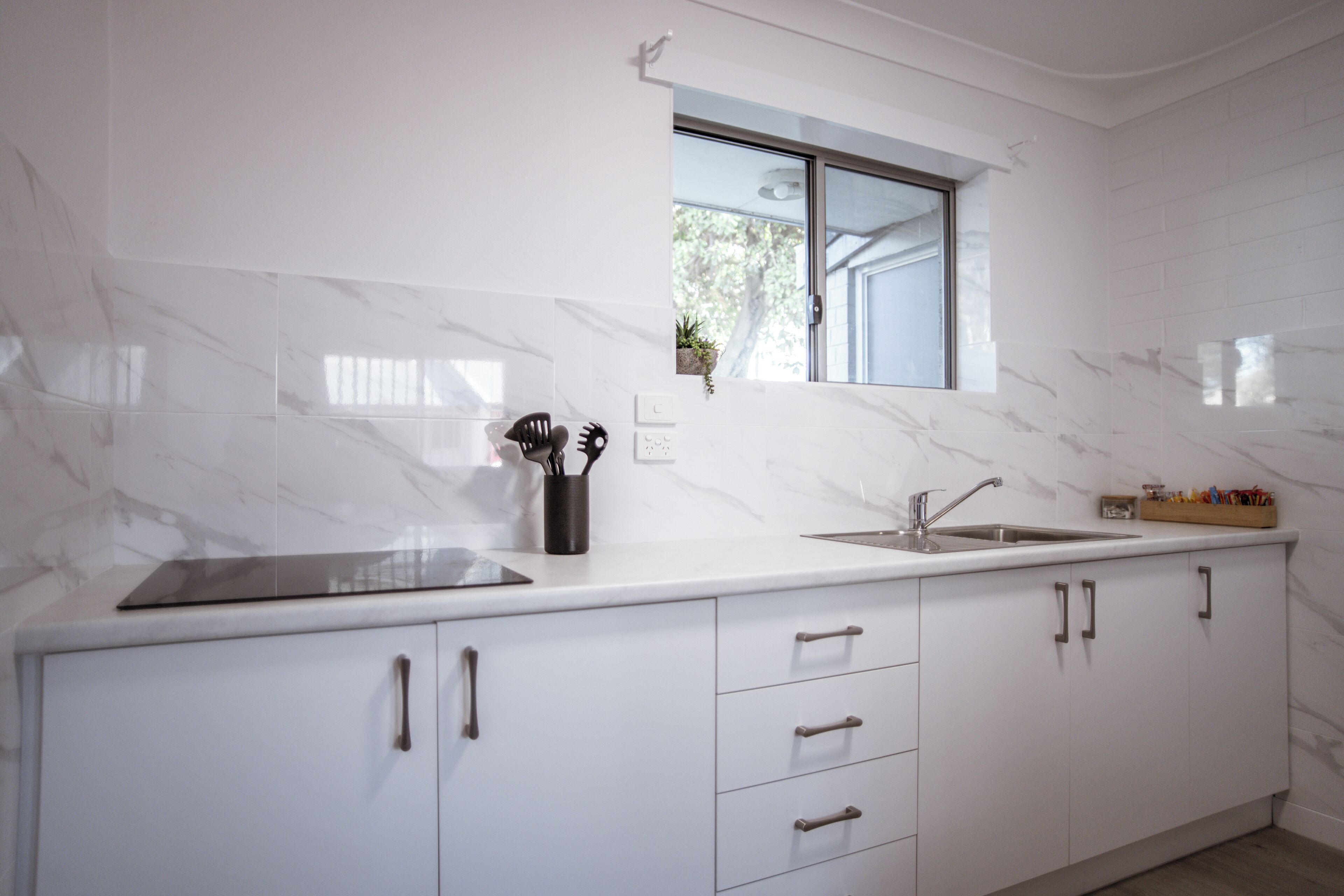 A modern kitchen with white marble countertops, a built-in sink, and a window above the sink.