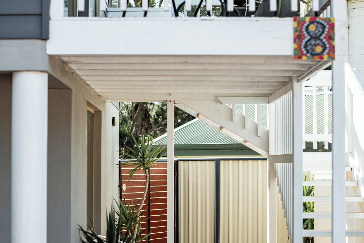 A covered outdoor area with a white railing, a potted plant, and a staircase leading to a second level.