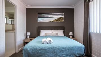 A hotel room with a bed, a painting of a beach, and a window with curtains.