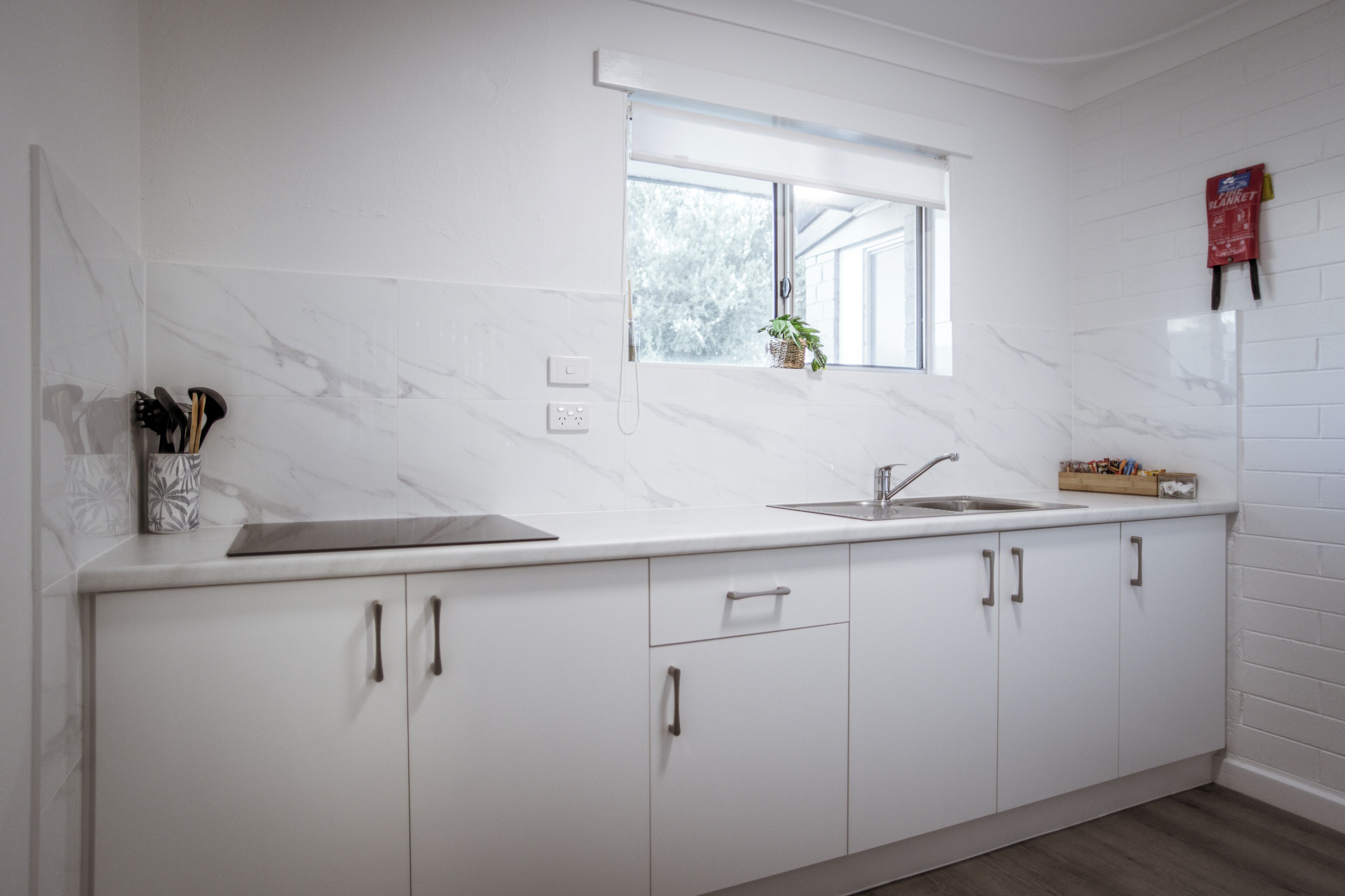 A modern kitchen with white cabinets, a marble backsplash, a window with a view, and a small plant on the windowsill.